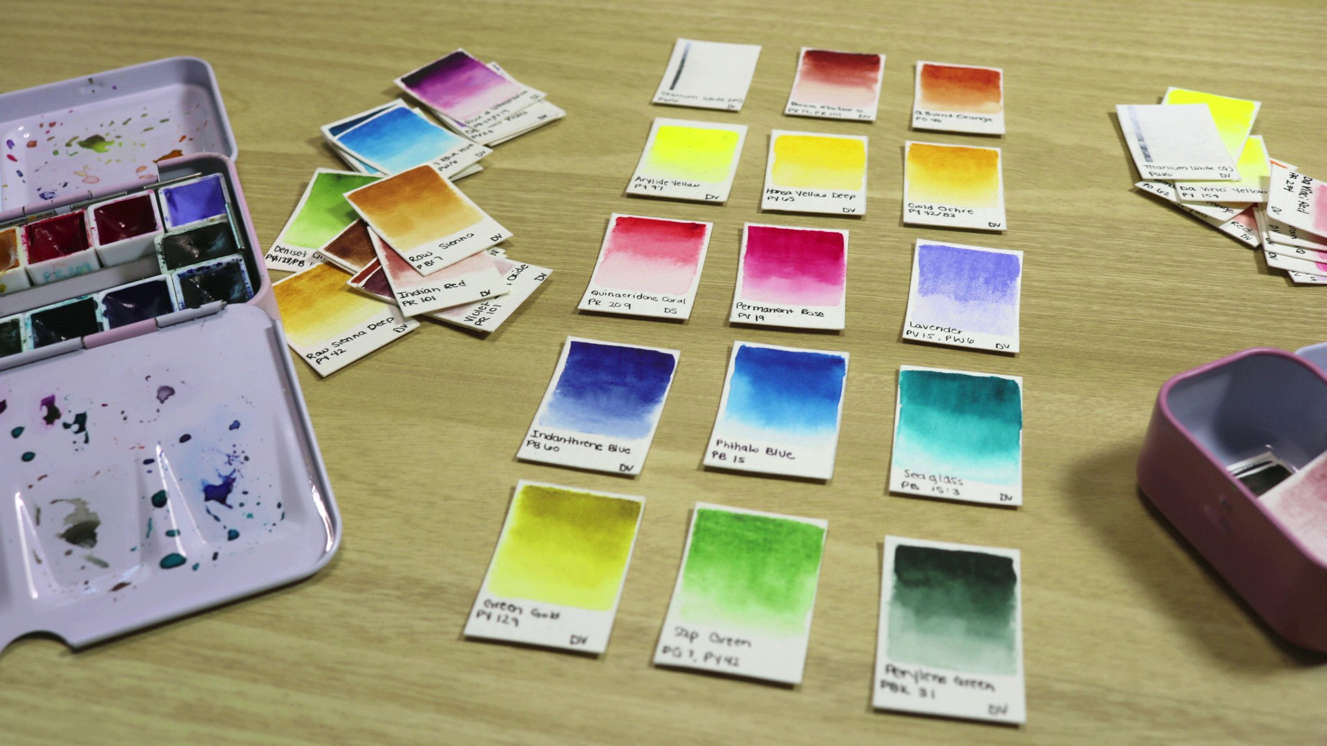 Swatches of various differnt watercolor paints are arranged on a desk