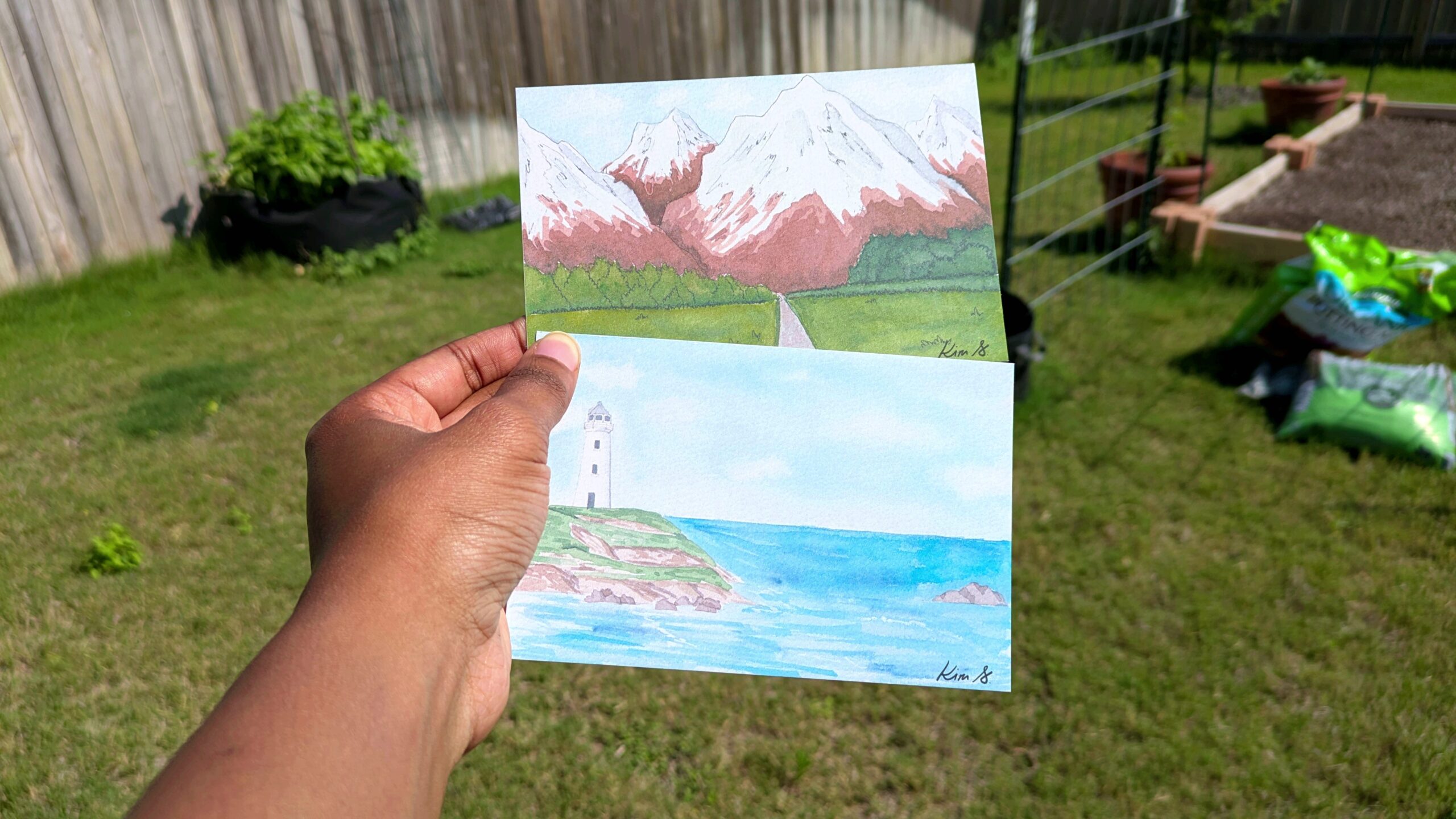 A hand holds two postcards from Qetsi Creates shop